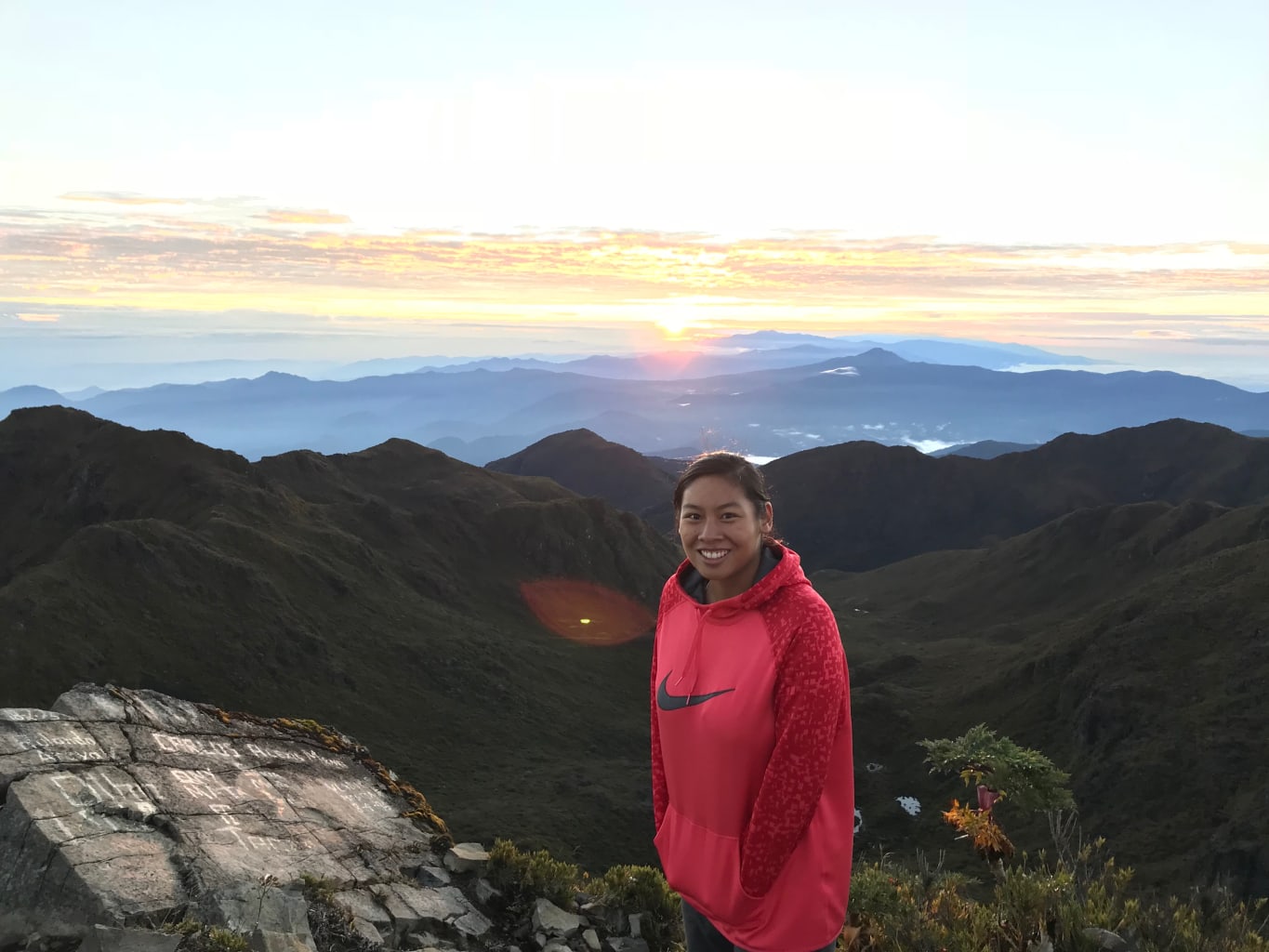 A student on a mountain with a view of a sunset in the background.
